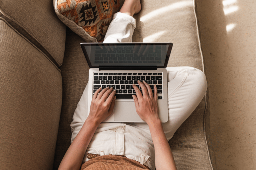 A relaxed person sitting on a couch ordering cannabis from a laptop
