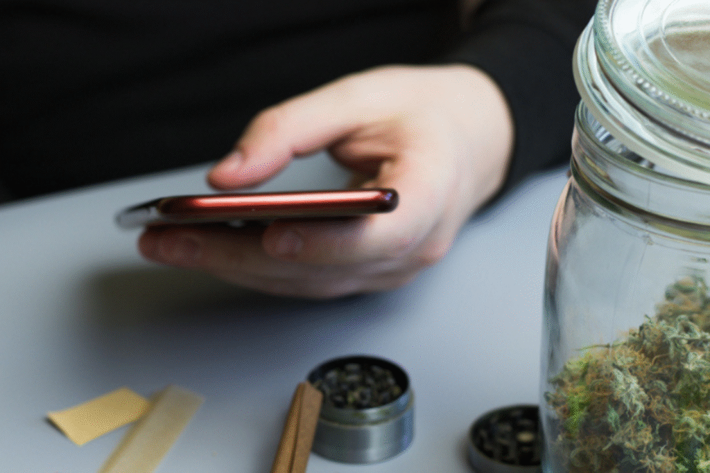 Person using smartphone with marijuana products on table.